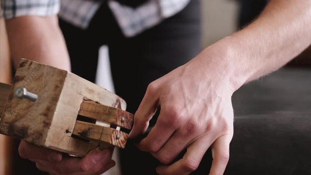 A craftsman is making a leather belt. The master is cutting the sheet of leather with a strap cutter.
