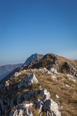 Foreground rocks with dry grass and red moss, narrow ridge at the top of the mountain, colorful autumn forest and impressive summit