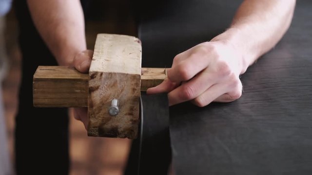 A craftsman is making a leather belt. The master is cutting the sheet of leather with a strap cutter.