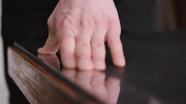 A tanner is cutting black leather sheet with a razor and metre. The master is making a leather belt for men.