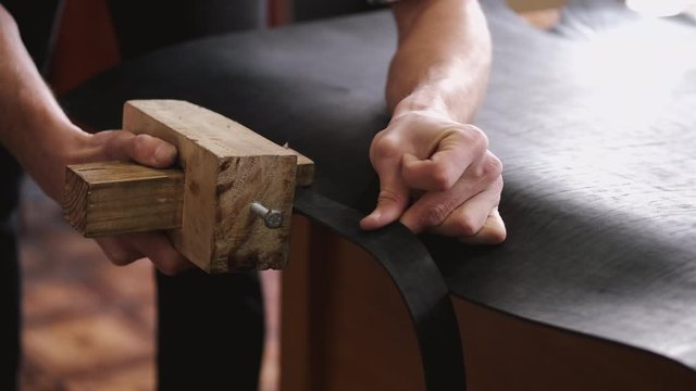 A craftsman is making a leather belt. The master is cutting the sheet of leather with a strap cutter