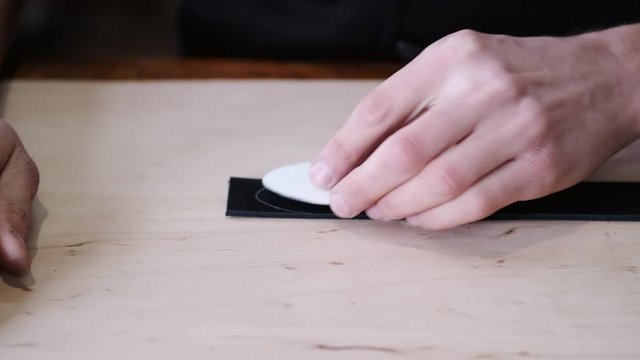 A leather craftsman is marking the end of a belt tail. The tanner is cutting the tail with scissors.