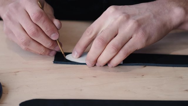 A leather craftsman is marking the end of a belt tail. The tanner is cutting the tail with scissors.