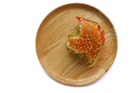 Top view of a partially eaten burger on a round wooden plate, isolated on white background. - Powered by Adobe