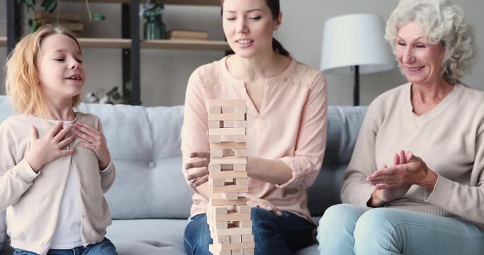 Happy three 3 age generations women family having fun playing jenga board game together. Cheerful young adult mom laughing enjoying funny leisure activity with old grandma and kid grandchild at home.