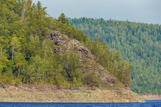 Beautiful landscape. Zeya reservoir, Amur region. A beautiful rocky shore with tall green trees goes into the calm blue waters of the reservoir.