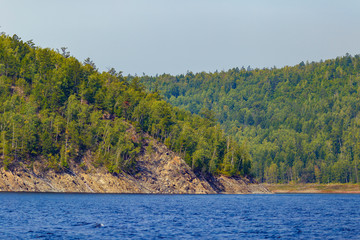 Beautiful landscape. Zeya reservoir, Amur region. A beautiful rocky shore with tall green trees goes into the calm blue waters of the reservoir.