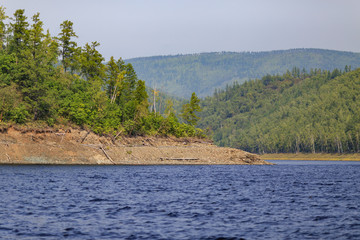 Beautiful landscape. Zeya reservoir, Amur region. A beautiful rocky shore with tall green trees goes into the calm blue waters of the reservoir.