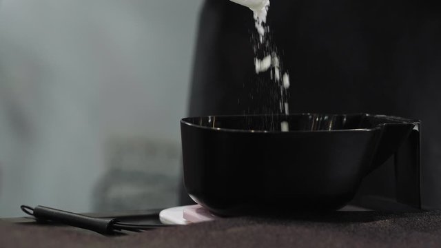 Hair dye powder is poured into a black bowl in close-up