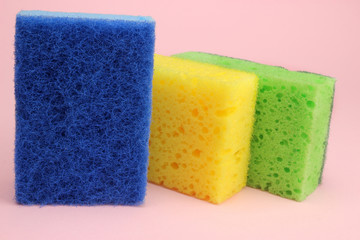 Colored sponges for dishes or home cleaning on a pink background