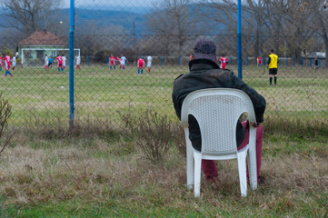 A fan of a local football club watches a game from a plastic chair