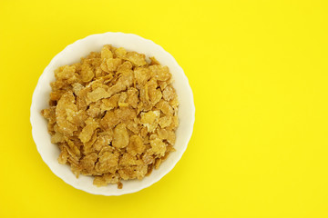 Cornflakes in a white plate on a yellow background, the view from the top