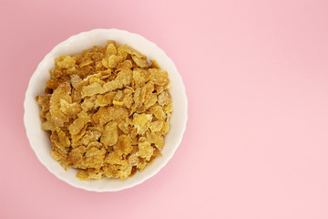 Cornflakes in a white plate on a pink background, the view from the top