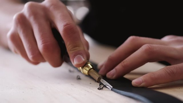 A leather craftsman is cutting the edges of a belt. The master is using an edge beveler tool.