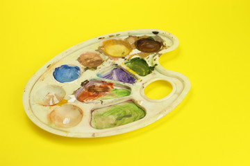 Palette with colors on a yellow background, the artist 's workplace