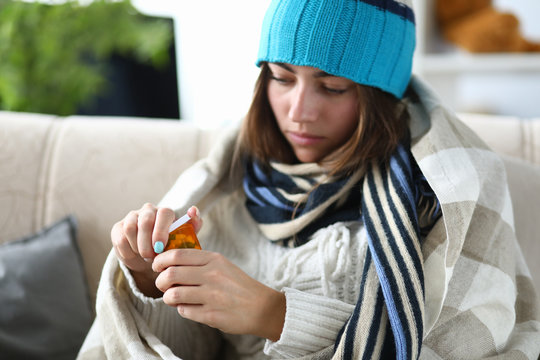 Close-up Of Ill Woman Opening Bottles With Medication. Sickness Female Person Wrapped Up In Blanket On Sick Leaves At Home. Sickness And Treatment Concept