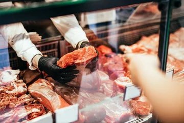 Fotobehang Close up on butcher's hands in gloves working in butchery. © hedgehog94