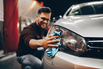 Young man washing his car in the evening at car wash station using high pressure water.