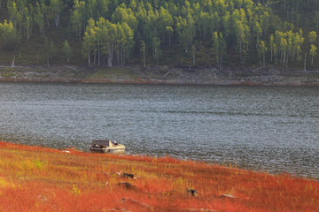 Obraz na płótnie Canvas Beautiful landscape. Zeya reservoir, Amur region. A metal boat stands on the shore of a picturesque beach with red grass on a background of blue water and green hills