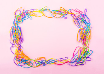 Colorful rubber bands and clips frame on pink paper background. Flat lay