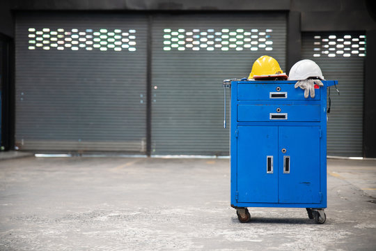 Blue metal tool cabinet with safety helmets, glove, document pad on the cabinet with garage background. Automobile repair service.