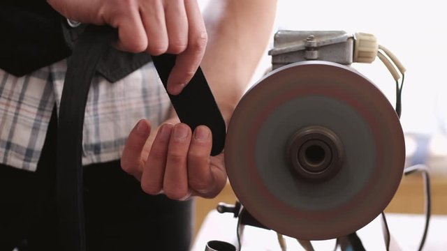 A craftsman is sharpening the edges of a belt on a special machine. The leather master is making a men's leather belt manually.