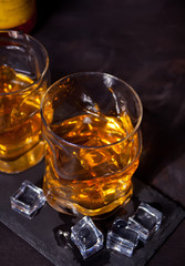 Two glasses of whiskey with ice on a black table.
