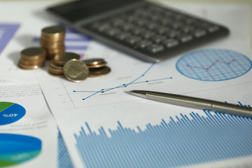 Close-up view of paper with business graphs and diagrams. Calculator and stack of coins on document. Statistics and accounting. Finance and economy growth concept