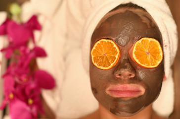Top view of woman applying skin cleansing facial pack. Female person in mask with piece of orange on eyes on spa treatments. Beauty and relaxation concept