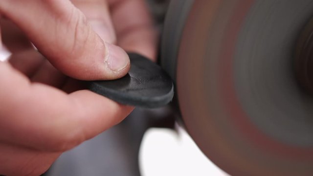 A craftsman is sharpening the edges of a belt on a special machine. The leather master is making a men's leather belt manually.