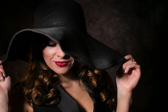 Colour portrait of beautiful female looking down while holding floppy hat on her head