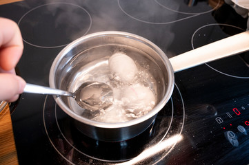 zwei hühner eier werden mit einem löffel in einen kochtopf mit kochendem wasser gelegt