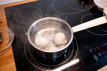 zwei hühner eier werden mit einem löffel in einen kochtopf mit kochendem wasser gelegt