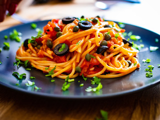 Pasta puttanesca with tomato sauce, anchovies, chilli, capers and olives on wooden table