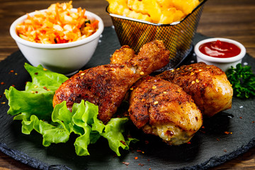Roast chicken drumsticks with french fries on black stone board