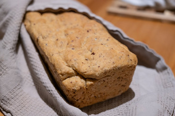 Frisches selbstgebackenes brot aus einer kastenform leigt eingehüllt in ein graues tuch auf einem holztisch