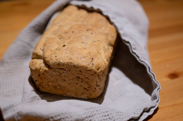 Frisches selbstgebackenes brot aus einer kastenform leigt eingehüllt in ein graues tuch auf einem holztisch