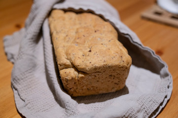 Frisches selbstgebackenes brot aus einer kastenform leigt eingehüllt in ein graues tuch auf einem holztisch