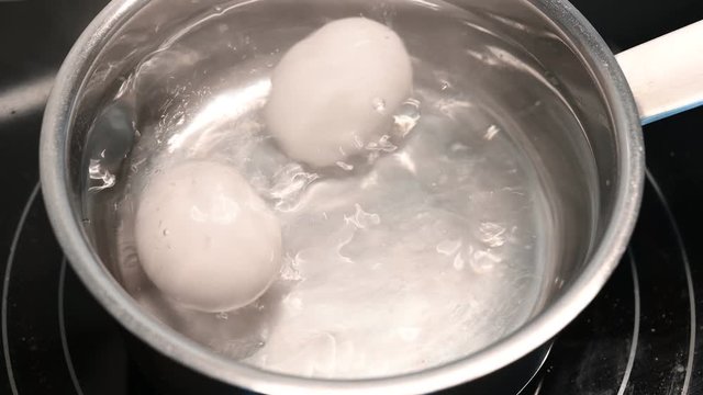zwei fr&uuml;hst&uuml;ckseier liegen in kochendem wasser auf dem herd in einem topf