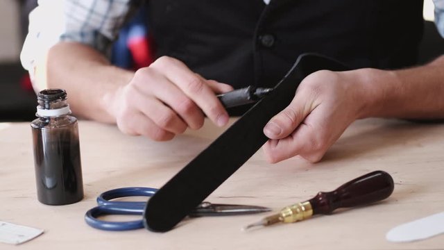 A leather master is dying leather belt edges. A craftsman is making hand-made men's leather belt.