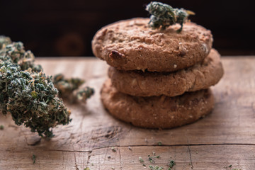 three cookies with marijuana lie on top of each other on a wooden board. Near big bud cannabis.