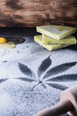 The process of making cannabis pastries. raw egg, rolling pin, traces of marijuana leaves on flour, and tiles hashish oil.