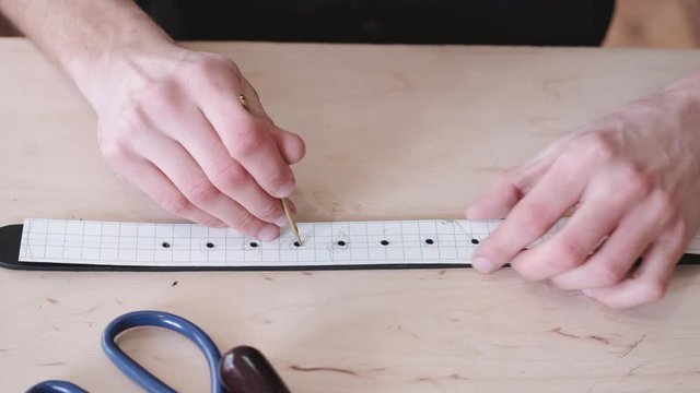 A leather craftsman is making holes in a hand-made belt. The tanner is using a mallet and a hole punch.