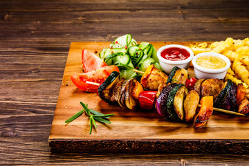 Grilled shashlik and French fries on wooden board