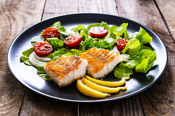 Fish dish - fried cod fillet with vegetables on wooden table