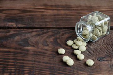 Phial with herbal tablets on wooden background with copy space
