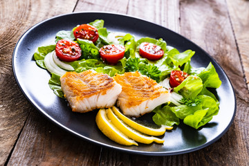 Fish dish - fried cod fillet with vegetables on wooden table