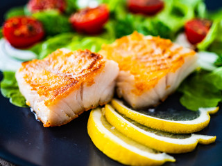 Fish dish - fried cod fillet with vegetables on wooden table