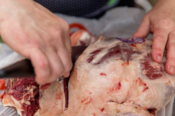 Hands with knives butcher the carcass of meat. Close-up.