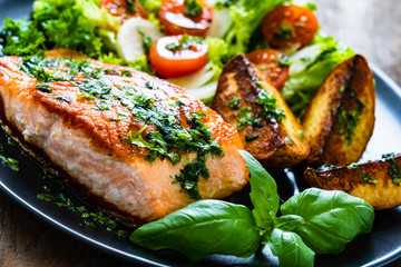 Fried salmon steak with potatoes and vegetables on wooden table